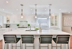 a large kitchen with white cabinets and an island in the middle is surrounded by four bar stools