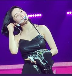 a woman in black dress holding a cell phone to her ear and singing on stage