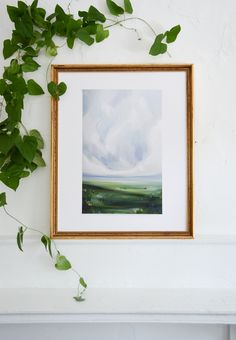 a painting is hanging on the wall next to a green leafy plant and some white walls