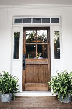 two potted plants are sitting on the front step of a house with a wooden door