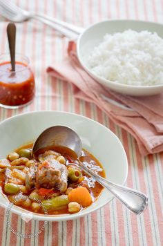 a bowl filled with meat and vegetables on top of a table next to white rice