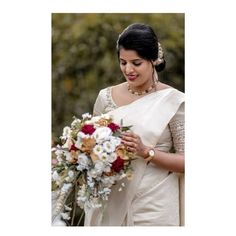 a woman in a white sari holding a bouquet of flowers and looking at the camera