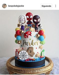 a spiderman themed birthday cake on a gold plated stand with balloons and decorations