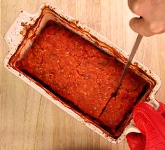 a person cutting into a square casserole dish with a red spatula in it