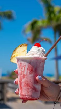 a person holding up a drink with ice cream and a pineapple on the top