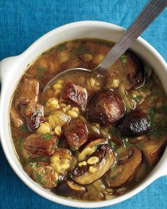 a bowl of soup with mushrooms and corn on a blue table cloth next to a spoon