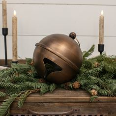 a table topped with candles and a large metal ball on top of evergreen leaves next to a candle holder