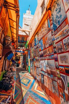 an alley way with many pictures on the wall and colorful rugs in front of it