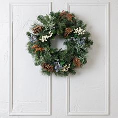 a wreath hanging on the wall with pine cones and berries