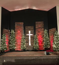 a church stage decorated for christmas with lighted trees and brick pillars on either side of the stage