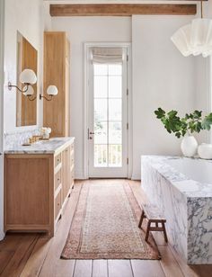 a white bathroom with marble counter tops and wooden cabinets, along with a plant in the corner