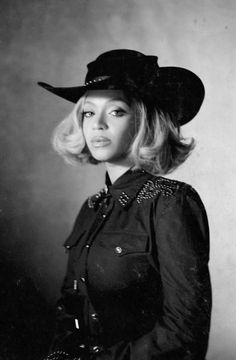 a black and white photo of a woman wearing a cowboy hat with her hands in her pockets