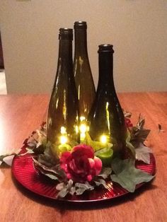 three wine bottles sitting on top of a red plate with lights in the bottle tops