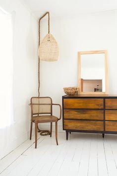 a room with a dresser, mirror and chair next to a lamp on the wall