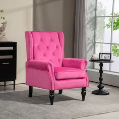 a bright pink chair sits in the corner of a room with a gray rug and black side table