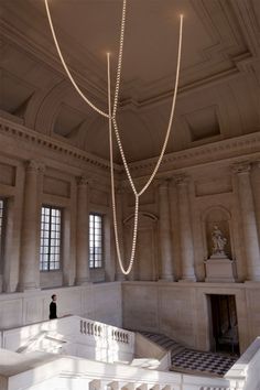 a chandelier hanging from the ceiling in a large room with columns and windows