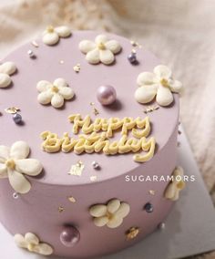 a purple cake with white flowers and the words happy birthday written on it is sitting on a plate