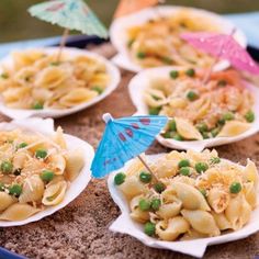 several plates of pasta and peas with umbrellas on the sand in front of them