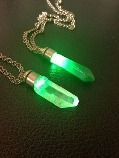 two necklaces with green lights on them sitting on a black surface next to a silver chain