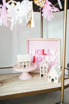 a table topped with pink and white paper houses on top of a wooden table next to a cake plate