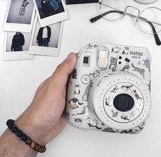 a person holding up a camera on top of a table with pictures and other items