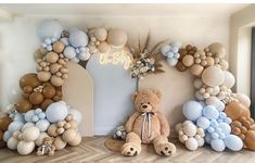 a teddy bear is sitting in front of balloons on the wall and an arch that says welcome