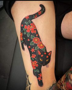 a black cat with red flowers on it's leg is standing in front of a tattoo