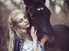 a woman is standing next to a horse and hugging it's face with her eyes closed