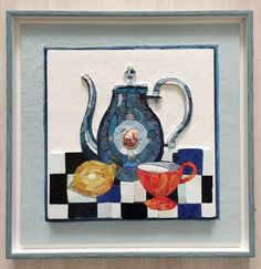 a blue teapot and two cups on a checkered table cloth with a silver frame