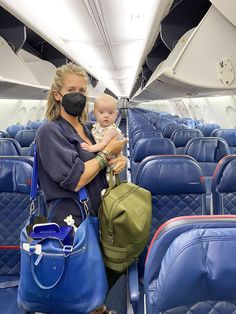 a woman holding a baby wearing a face mask while sitting on an airplane with blue seats