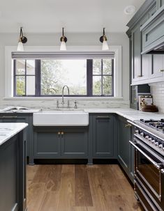 a kitchen with gray cabinets and white counter tops, wood floors, and an open window