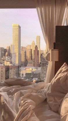 an unmade bed in front of a window overlooking the city