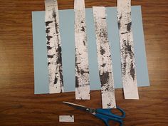 the paper is cut out to look like birch trees and scissors are next to it