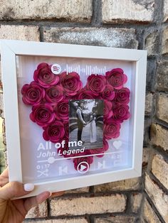 a person holding up a framed photo with flowers in the shape of a heart and text all of me john legend