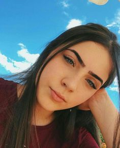 a woman with long hair and brown eyes posing for a photo in front of the sky