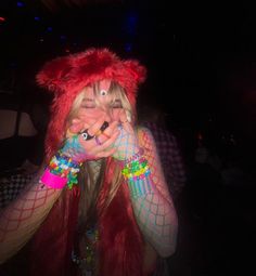 a woman with red hair and colorful makeup covers her face as she poses for the camera