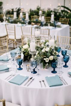 the table is set with blue and white place settings, silverware, candles, and flower centerpieces