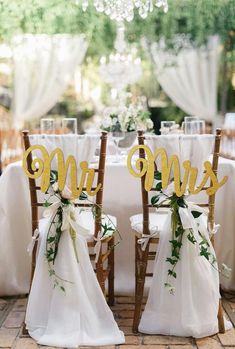 two chairs with sashers and bows on them sitting in front of a table set for a wedding