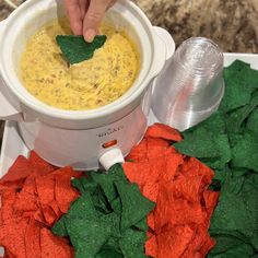 a person dipping tortilla chips into a white bowl filled with yellow and green dip