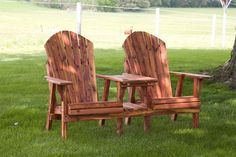 two wooden chairs sitting in the grass near a tree