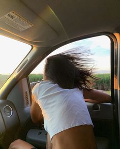 a woman sitting in the driver's seat of a car with her hair blowing in the wind