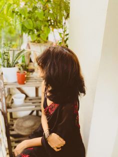 a woman sitting on a chair in front of a potted plant next to a wall