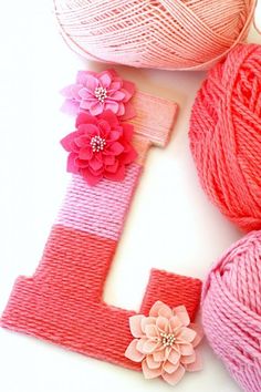 yarn and flowers are arranged next to the letter h, which is knitted in pink