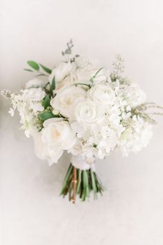 a bridal bouquet with white flowers and greenery on the bottom is photographed against a wall