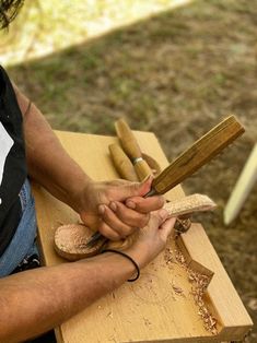 a man is carving something with wood shavings on a wooden table in the park