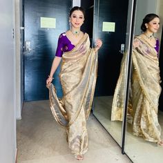 a woman is standing in front of a mirror wearing a sari and holding a purse