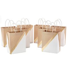 four white and gold paper bags with handles on each side are lined up against one another