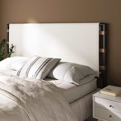 a bed with white linens and pillows in a brown room next to a window