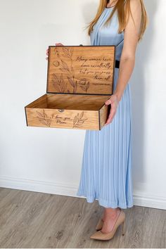 a woman in a blue dress holding a wooden box with writing on the lid and inside