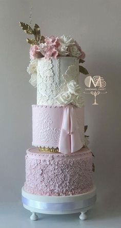 a three tiered wedding cake with pink and white flowers on the top, sitting on a stand